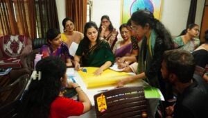 Group of Indian colleagues gathered around a table, working on a large yellow poster in a meeting room during a workshop.",