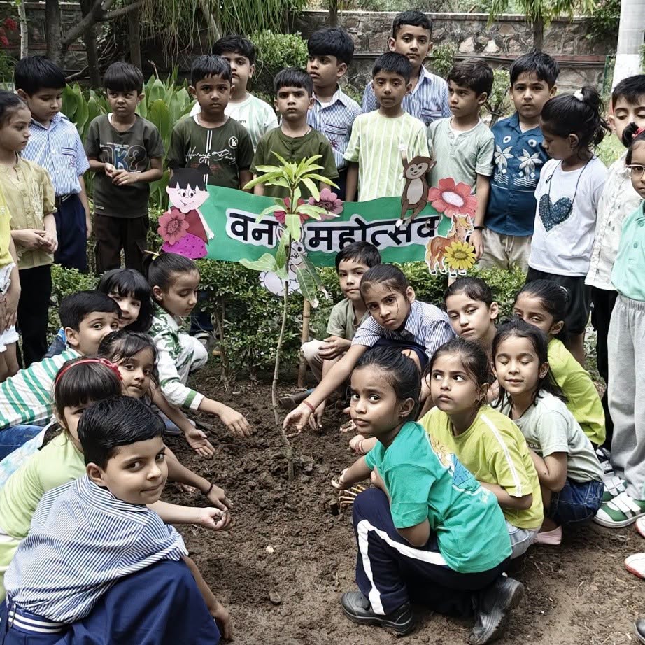Group of smiling schoolchildren planting a sapling together outdoors, with a colorful banner reading 'वन महोत्सव' in the background.